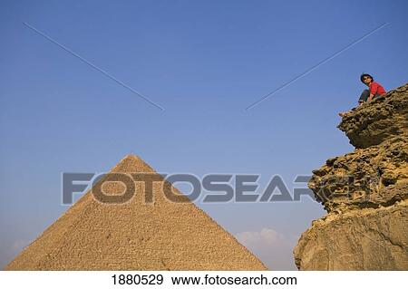 Stock Photo - Woman On Rocky Outcrop Looking Over Pyramids. Fotosearch