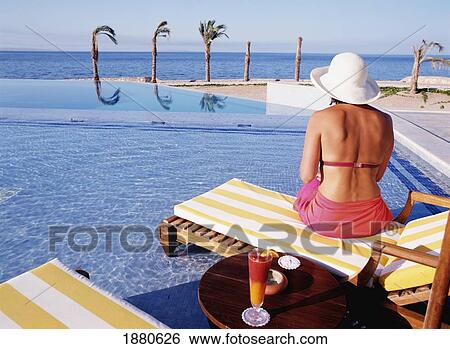 Stock Photograph - Woman On Sun Lounger At Pool By Sea. Fotosearch