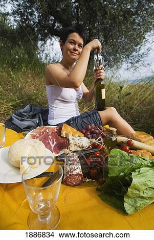 Picture - Woman Opening Bottle Of Wine In Preparation For Picnic Under Olive Trees. Fotosearch