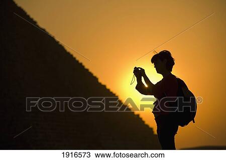 Stock Image - Woman Photographing Pyramids At Dusk. Fotosearch