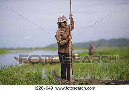 Stock Photo - Woman poling a boat on the Kamping Puoy Reservoir; Battambang, Cambodia. Fotosearch