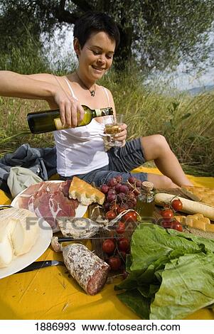 Stock Image - Woman Pouring Bottle Of Wine In Preparation For Picnic Under Olive Trees. Fotosearch