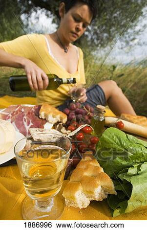 Stock Photograph - Woman Pouring Bottle Of Wine In Preparation For Picnic Under Olive Trees. Fotosearch