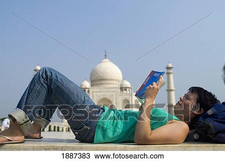 Stock Image - Woman Reading Guide Book In Front Of The Taj Mahal, Side View. Fotosearch