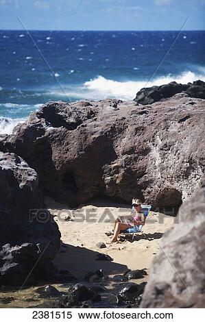 Stock Photography - Woman reading in a secluded piece of beach at Ho'okipa Beach Park; Paia, Maui, Hawaii, United States of America. Fotosearch