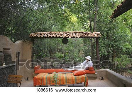 Stock Photograph - Woman Reclining On Chaise Lounge On A Patio In The Jungle. Fotosearch