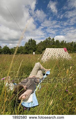 Stock Image - Woman Resting Beside Tent In Meadow. Fotosearch