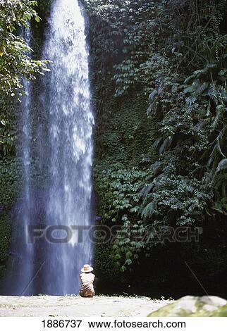 Stock Photo - Woman Sitting Beside Waterfall, Sendang Gila. Fotosearch