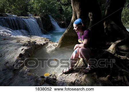 Stock Image - Woman Sitting By Small Waterfall; Luang Prabang, Laos. Fotosearch