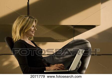 Stock Photo - Woman Sitting In A Chair On A Laptop, Toronto, Ontario. Fotosearch