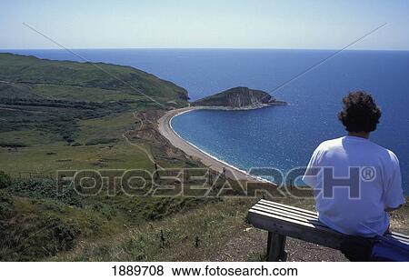Stock Photo - Woman Sitting On Bench By Coast, High Angle View. Fotosearch