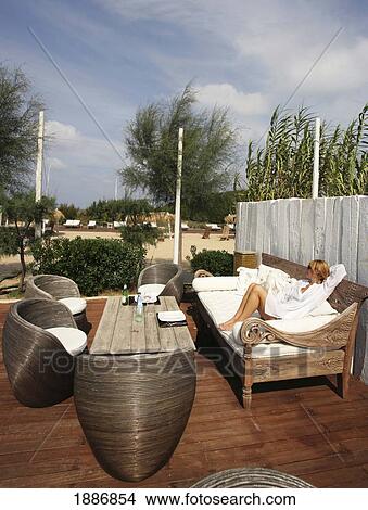 Picture - Woman Sitting On Outdoor Sofa On A Deck. Fotosearch