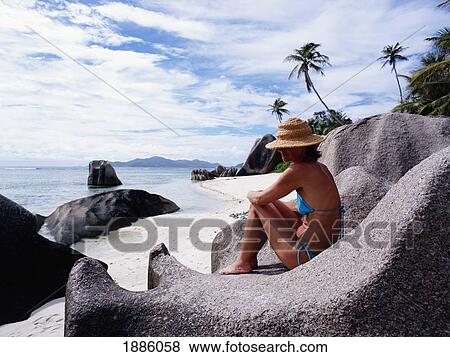 Stock Photo - Woman Sitting On Rocks On The Beach. Fotosearch