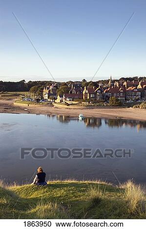Stock Image - Woman Sitting On Water's Edge; Alnmouth, Northumberland, England. Fotosearch