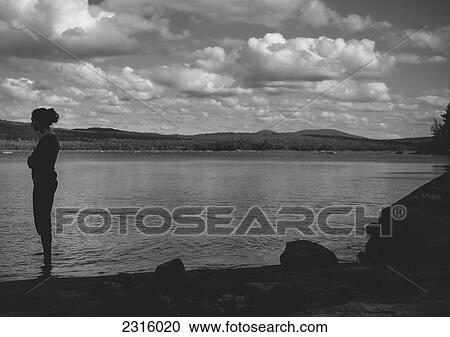 Stock Image - Woman Standing In A Lake With Arms Folded Under Dramatic Skies; Thetford Mines Quebec Canada. Fotosearch