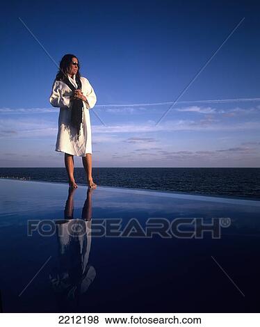 Woman standing in a spa robe on the edge of an infinity pool looking out over the ocean; Madeira, Portugal View Large Photo Image Stock Photo - Woman standing in a spa robe on the edge of an infinity pool looking out over the ocean; Madeira, Portugal. Fotosearch