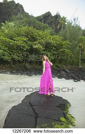 Stock Photograph - Woman standing on a large rock on the beach; Kauai, Hawaii, United States of America. Fotosearch