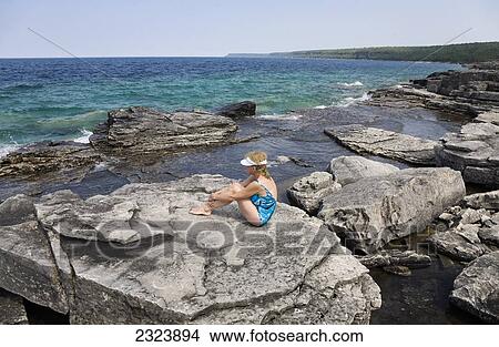 Woman sunbathing on a rocky beach overlooking Georgian Bay in Bruce Peninsula National Park; Ontario, Canada View Large Photo Image Picture - Woman sunbathing on a rocky beach overlooking Georgian Bay in Bruce Peninsula National Park; Ontario, Canada. Fotosearch