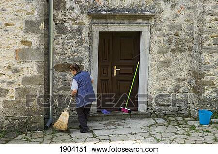 Stock Image - Woman Sweeping Street In Town Of Hum, Istria, Croatia. Fotosearch