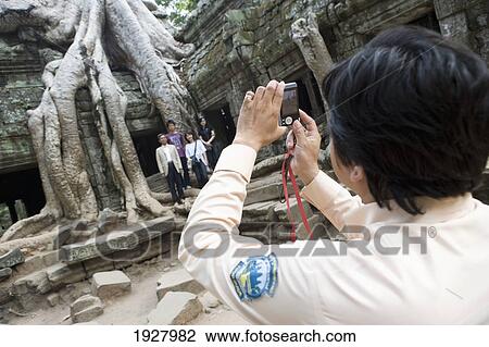 Stock Image - Woman Taking Photo Group Of People At Temple Of Ta Prohm, Siem Reap, Cambodia. Fotosearch