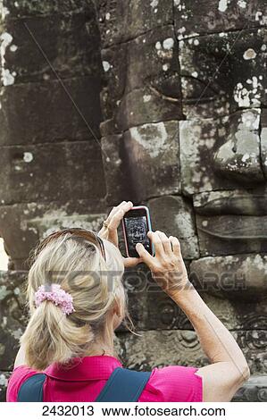 Woman taking picture with iphone of smiling face statue at Bayon Temple in Angkor Thom, near Angkor Wat; Siem Reap, Cambodia View Large Photo Image Stock Image - Woman taking picture with iphone of smiling face statue at Bayon Temple in Angkor Thom, near Angkor Wat; Siem Reap, Cambodia. Fotosearch