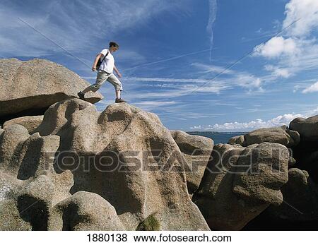 Stock Photo - Woman Walker Jumping Over Rock Formations, Low Angle View. Fotosearch