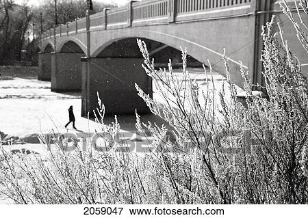 Stock Photo - Woman Walking On Frozen Assiniboine River Under Assiniboine Park Bridge On A Snowy Winter Day. Winnipeg, Manitoba, Canada.. Fotosearch