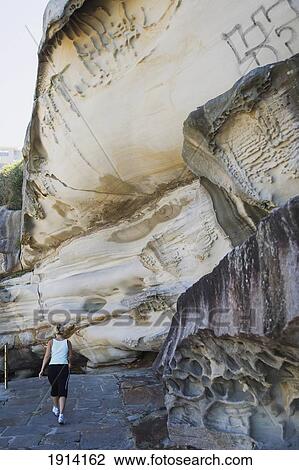 Stock Image - Woman Walking Past Cliff. Fotosearch