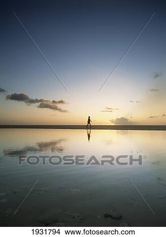 Picture - Woman Walking Past Shallow Pool Beside Brighton Beach On West Coast Of Barbados At Dusk.. Fotosearch