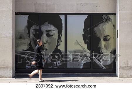 Stock Image - Woman walking past signs for a noodle bar; London, England. Fotosearch