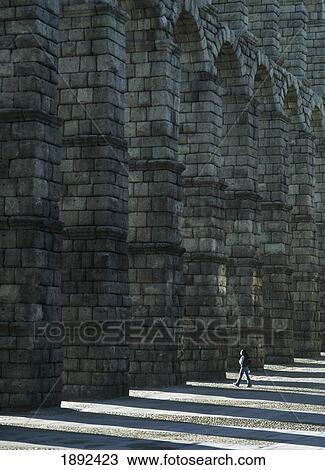 Stock Image - Woman Walking Through Arch Of Roman Aqueduct. Fotosearch