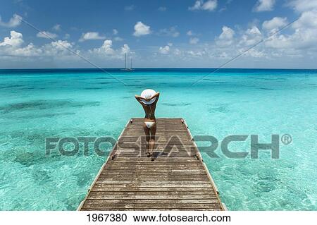 Stock Image - Woman Walking To End Of Tropical Ocean Pier, View From Behind.. Fotosearch
