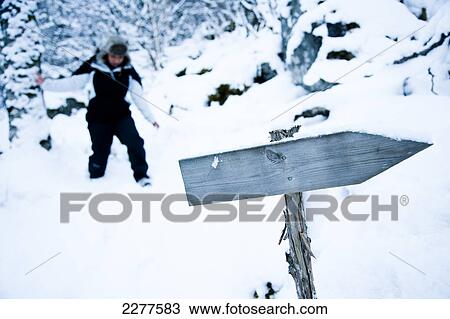 Stock Image - Woman walks along snowy footpath, past a signpost in an alpine winter scene with snow on a mountain; Ortnevik, Sognefjord, Norway. Fotosearch