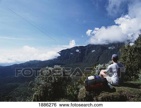 Stock Photograph - Woman With Backpack Sitting On Edge Of Mountaintop. Fotosearch