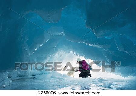 Stock Photograph - Woman with her pet dog inside a natural ice cave on frozen Lake Superior in winter; Ontario, Canada. Fotosearch