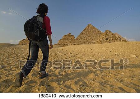 Stock Image - Woman With Rucksack Walking Towards Pyramids At Dusk. Fotosearch