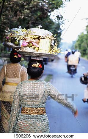 Woman ( Women ) In Embroidered Dress With Temple Offerings Walking Down A Road With Motorcyclists In The Distance. Ubud, Bali, Indonesia. View Large Photo Image Stock Photograph - Woman ( Women ) In Embroidered Dress With Temple Offerings Walking Down A Road With Motorcyclists In The Distance. Ubud, Bali, Indonesia.. Fotosearch
