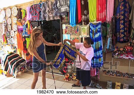 Stock Image - Women Downtown Looking At Textiles On Display; Todos Santos Baja California Sur Mexico. Fotosearch