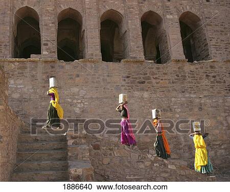 Stock Image - Women In Colorful Saris Carrying Boxes On Their Heads While Climbing Stairs. Fotosearch