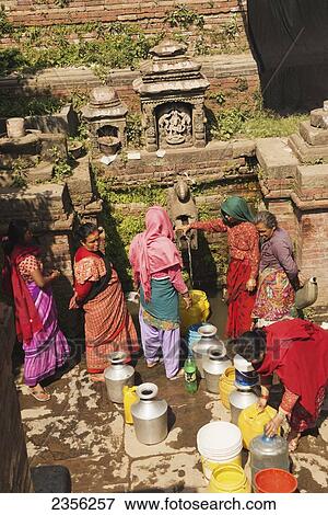 Stock Photo - Women in colourful saris fill up water containers from a water trough in an old tank; Bhaktapur, Nepal. Fotosearch