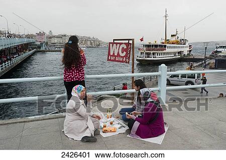 Stock Image - Women sitting and eating on a bridge overlooking the water; Istanbul, Turkey. Fotosearch
