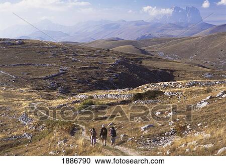 Stock Image - Women Walking Down Track Near Rocca Calascio With The Peak Of Corno Grande Behind. Fotosearch