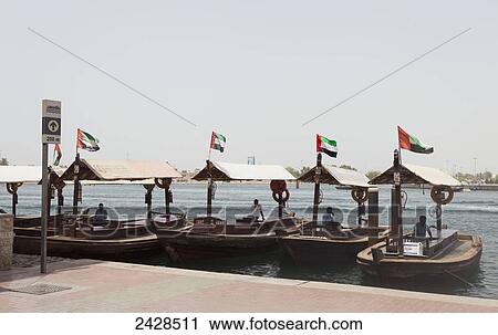 Wooden boats with the flag of the United Arab Emirates lined up along the waterfront; Dubai, United Arab Emirates View Large Photo Image Stock Image - Wooden boats with the flag of the United Arab Emirates lined up along the waterfront; Dubai, United Arab Emirates. Fotosearch