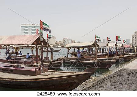 Wooden boats with the flag of the United Arab Emirates moored in a row along the shore; Dubai, United Arab Emirates View Large Photo Image Stock Photo - Wooden boats with the flag of the United Arab Emirates moored in a row along the shore; Dubai, United Arab Emirates. Fotosearch