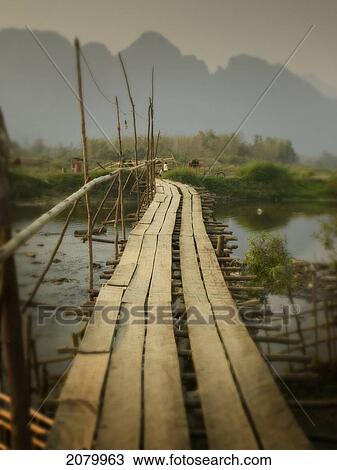 Stock Image - Wooden Bridge Over A River With Mountains In The Background; Vang Vieng Laos. Fotosearch
