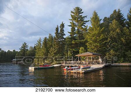 Stock Image - Wooden Docks With A Roof And Boats In The Water; Keewatin Ontario Canada. Fotosearch