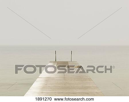 Stock Image - Wooden Pier On Misty Lake At Dawn. Fotosearch