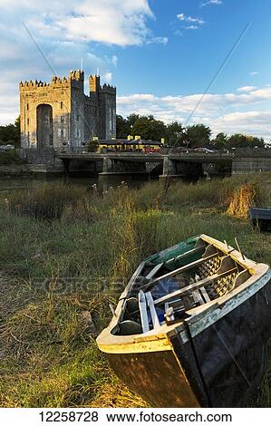 Stock Photo - Wooden row boat in grassy field with stone castle and bridge in background at sunset with blue sky and clouds; Bunratty, County Clare, Ireland. Fotosearch