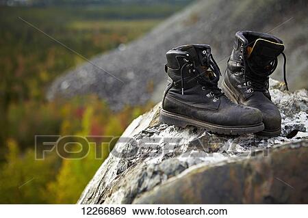 Stock Photo - Work boots on a rock with autumn coloured trees in the background; Quebec, Canada. Fotosearch