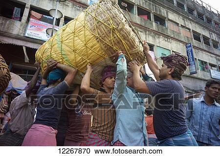 Stock Image - Workers carry large basket of vegetables; Kolkata, West Bengal, India. Fotosearch